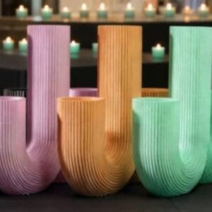 A collection of Luxe Triple Tealight Holders in black, lilac, sand orange, mint green, and soft white, arranged as a designer set with flickering tealights in the background.
